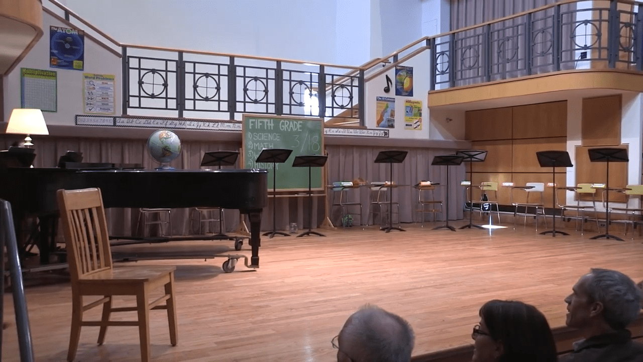 Empty school stage with piano and chairs.